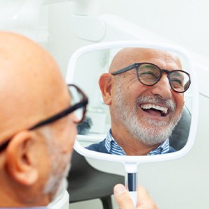 Man with glasses smiling at reflection in handheld mirror