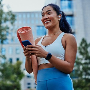 Smiling woman walking on park with workout mat