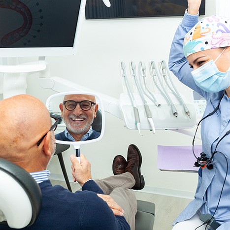 Older man looking at new dentures in Rogers while at the dentist’s office