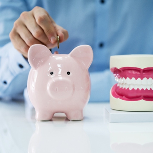 A man putting a coin in a piggy bank, which is next to a model jaw