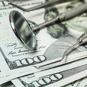 Dental tools laying on a stack of hundred-dollar bills