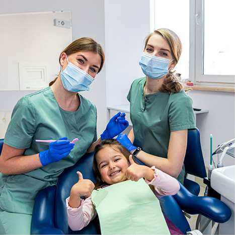 Two smiling Rogers dental team members with a young girl in the dental chair giving thumbs up
