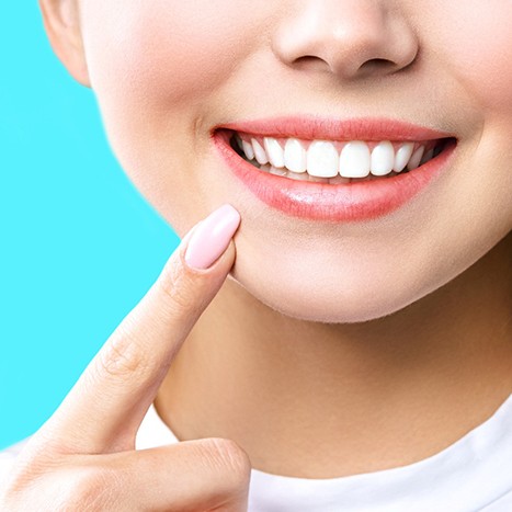 Nose-to-neck view of woman pointing to her bright smile with manicured nail