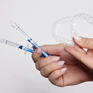 Hands holding custom-fitted trays and whitening gel applicator tubes