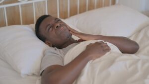 Man in bed holding mouth in pain. 